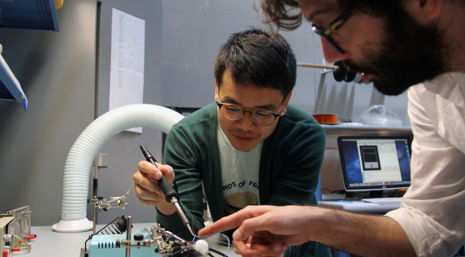 Faculty Casey Anderson assists /lab student Tim Kim with soldering.